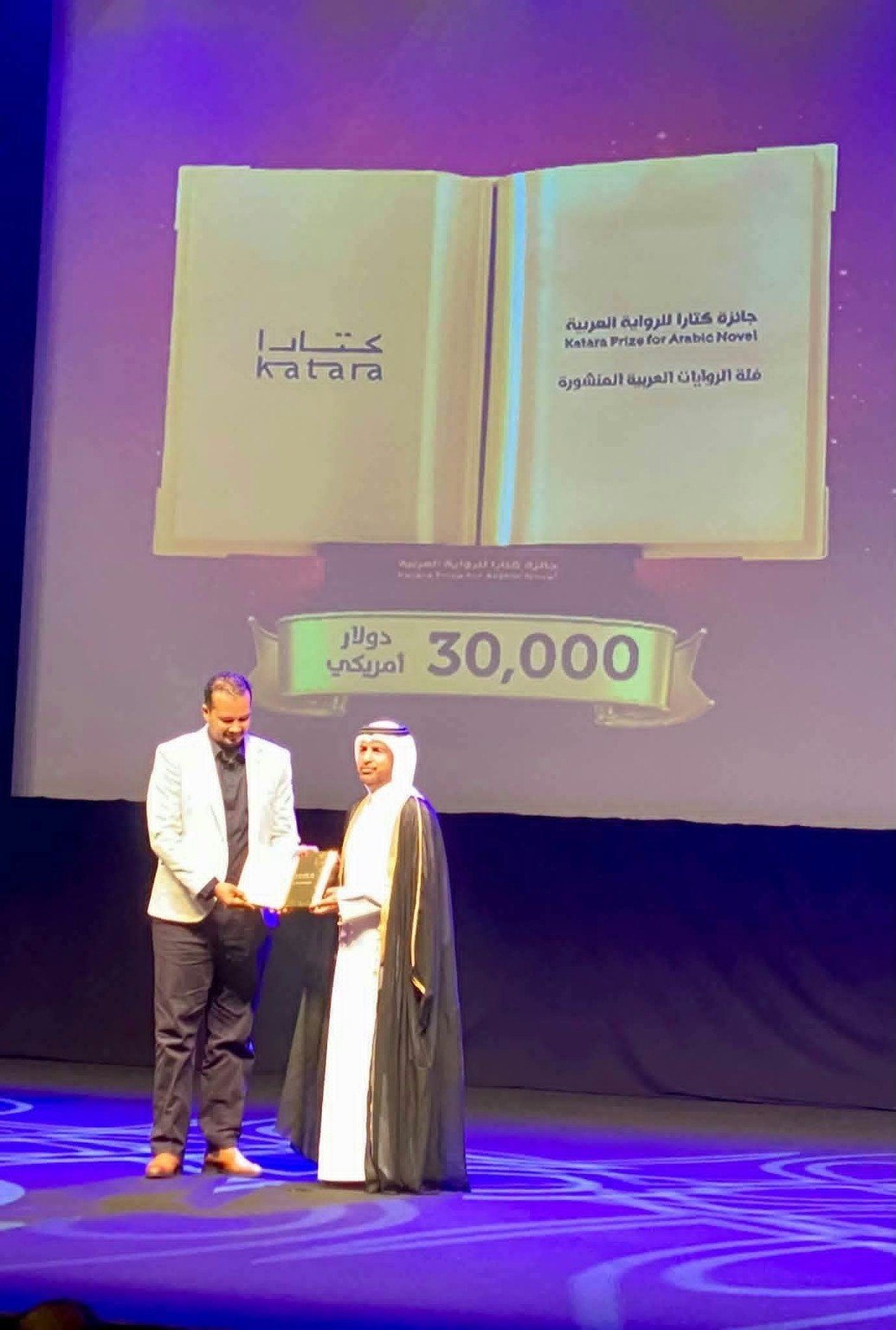 مشهد من حفل جائزة كتارا للرواية العربية، يتسلم فيه الروائي السوداني مهند رجب الدابي درع التكريم على المسرح.